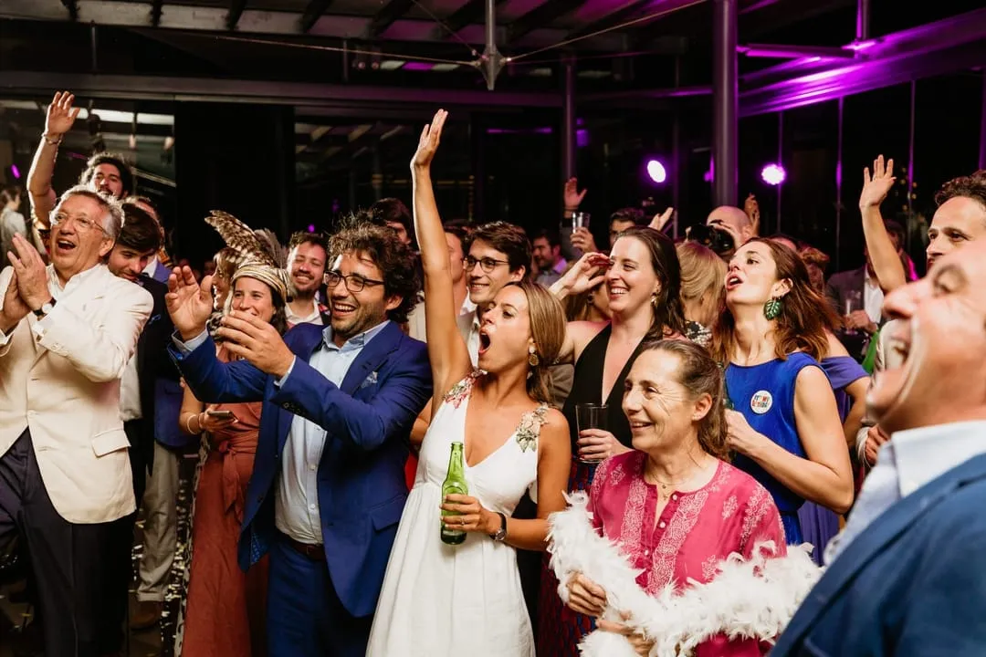 A massive crowd at a wedding clapping and throwing their hands in the air to the DJ's song