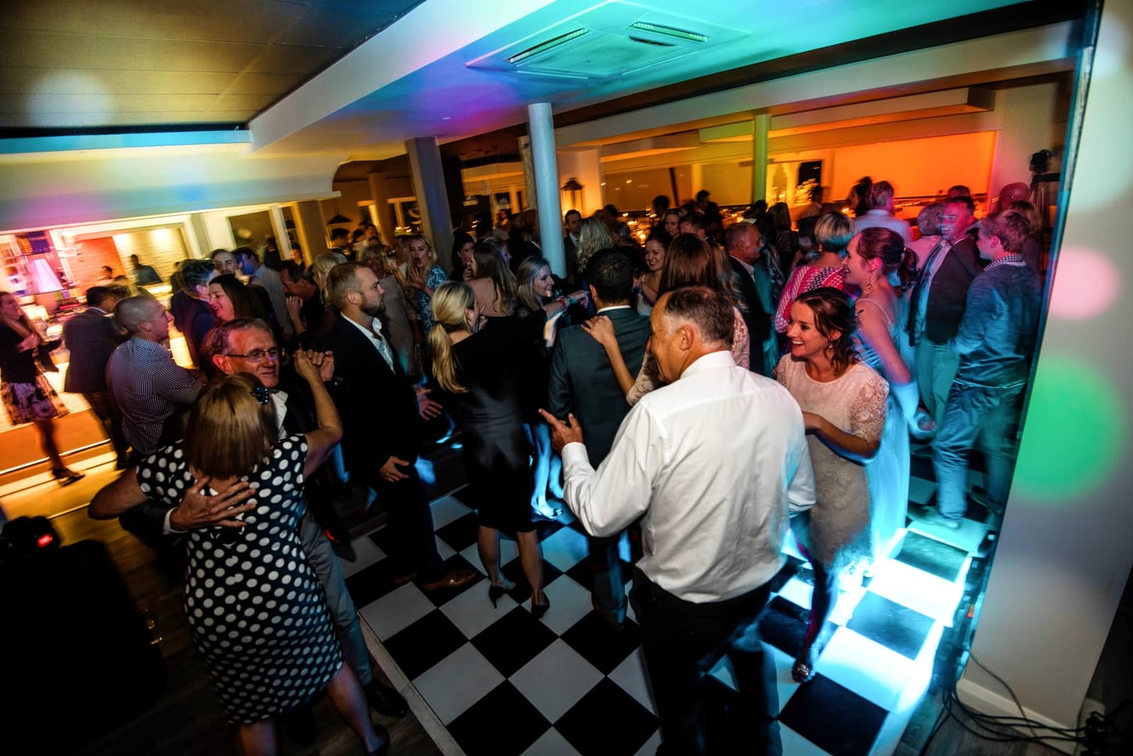 Wedding guests packing a black and white dance floor under coloured lights