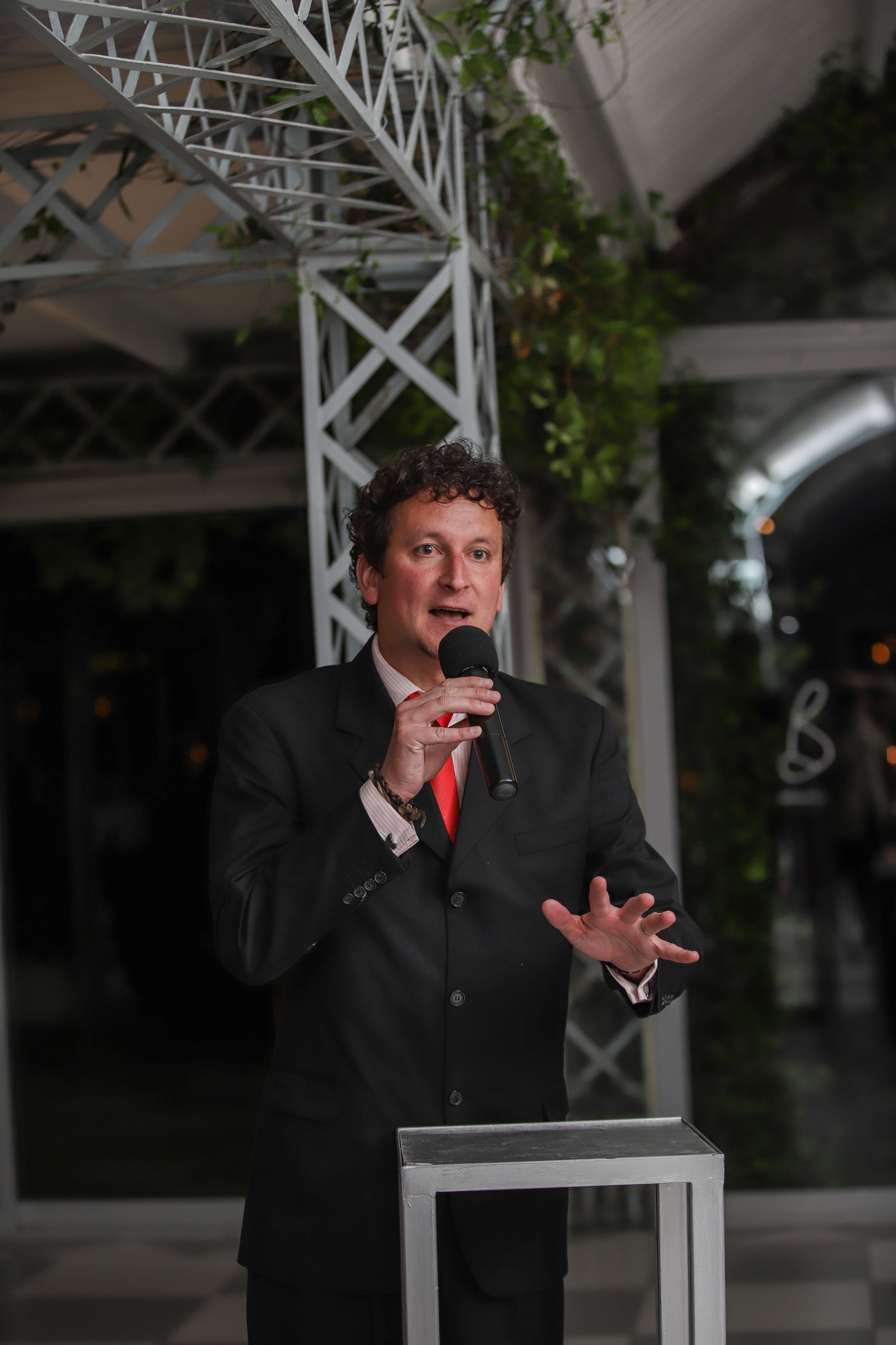 A man in a grey suit with a red tie giving a speech.