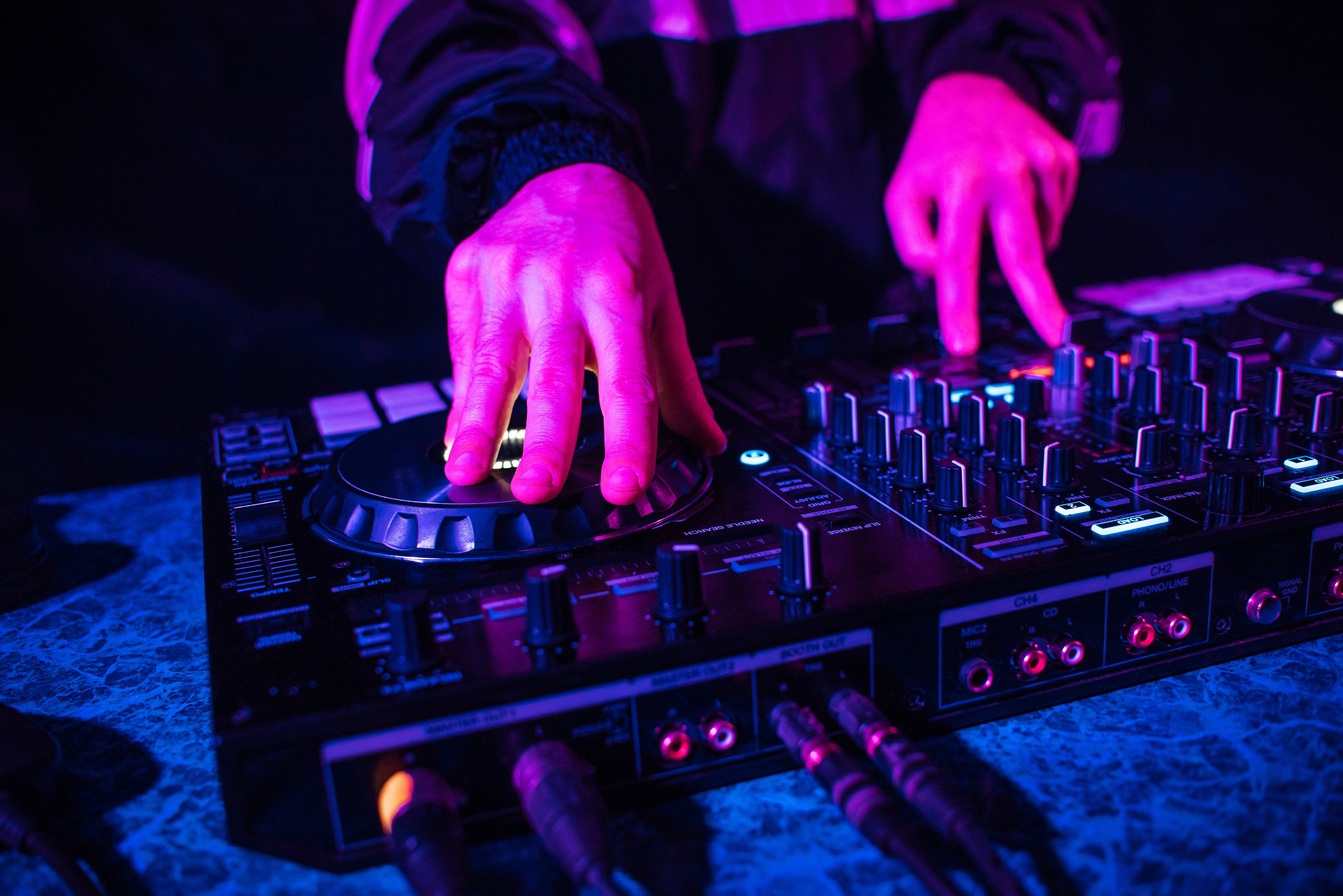Close-up of a DJ's hands on a controller's jog wheel and faders under pink and blue light