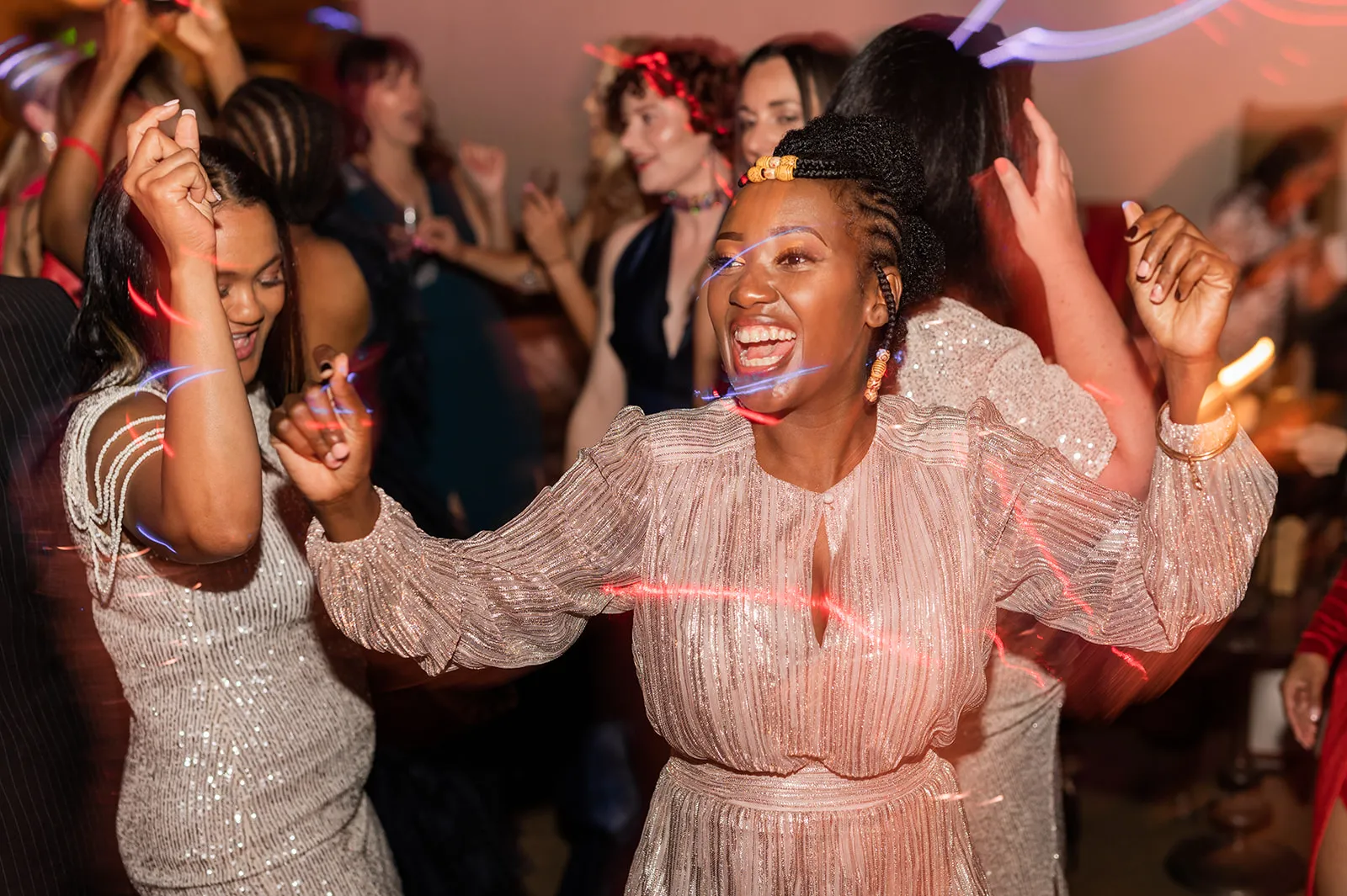 Woman in a shimmering pink dress laughing as she dances with friends on a party dance floor