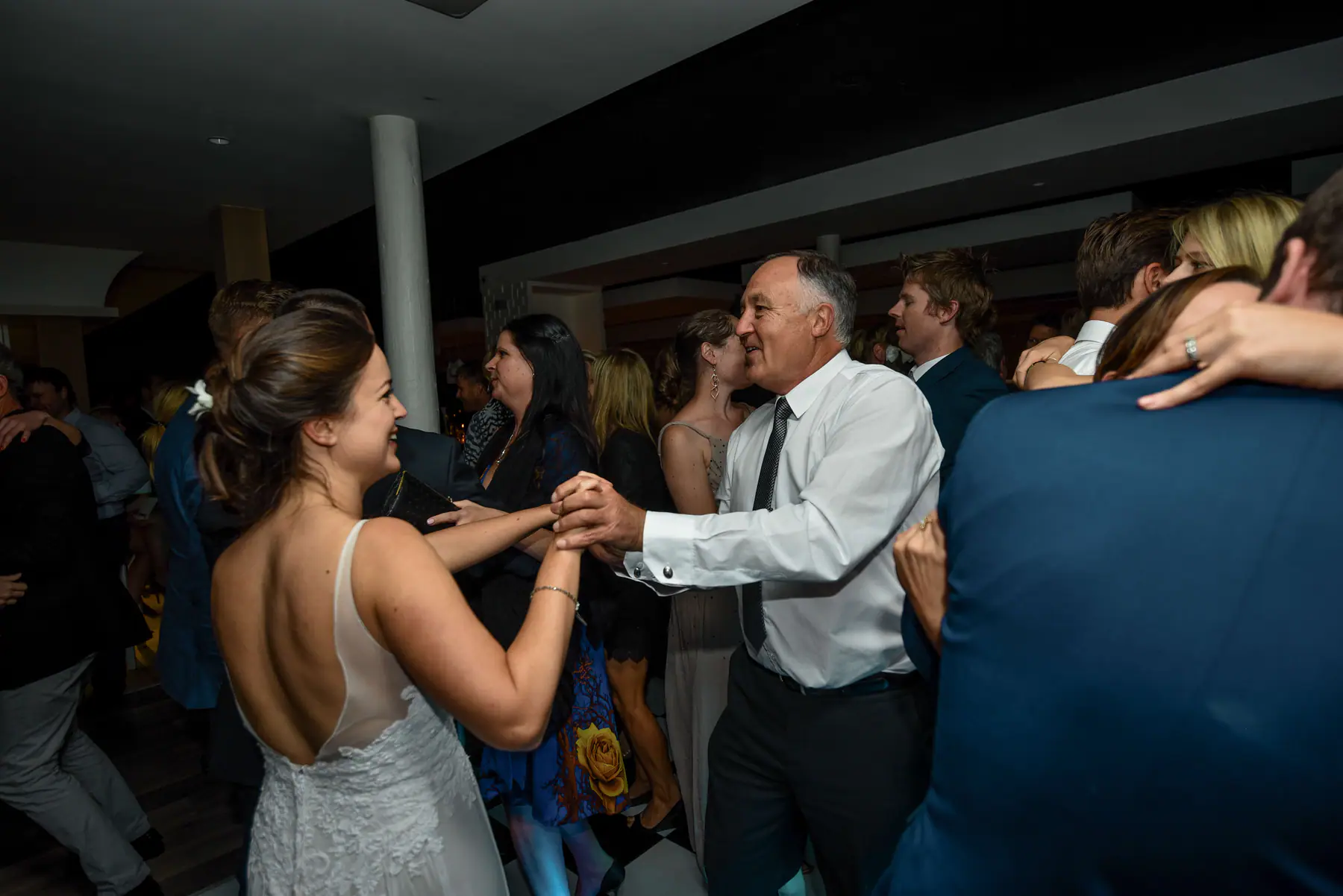 Karen holding hands with a grey-haired man in a white shirt and tie, both smiling, in a crowd of dancing guests