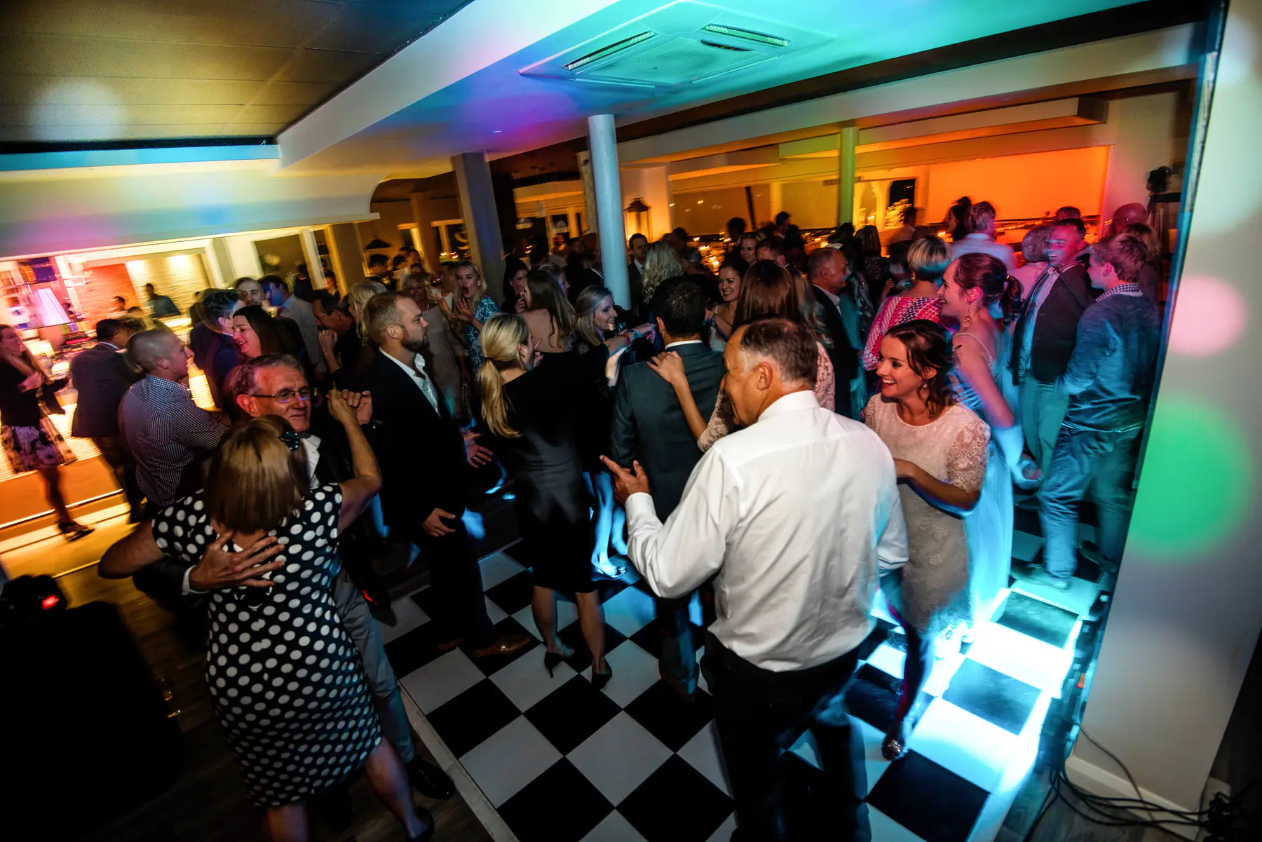 Couples dancing on a crowded black and white dance floor, a woman in polka dots in front and an amber-lit room behind