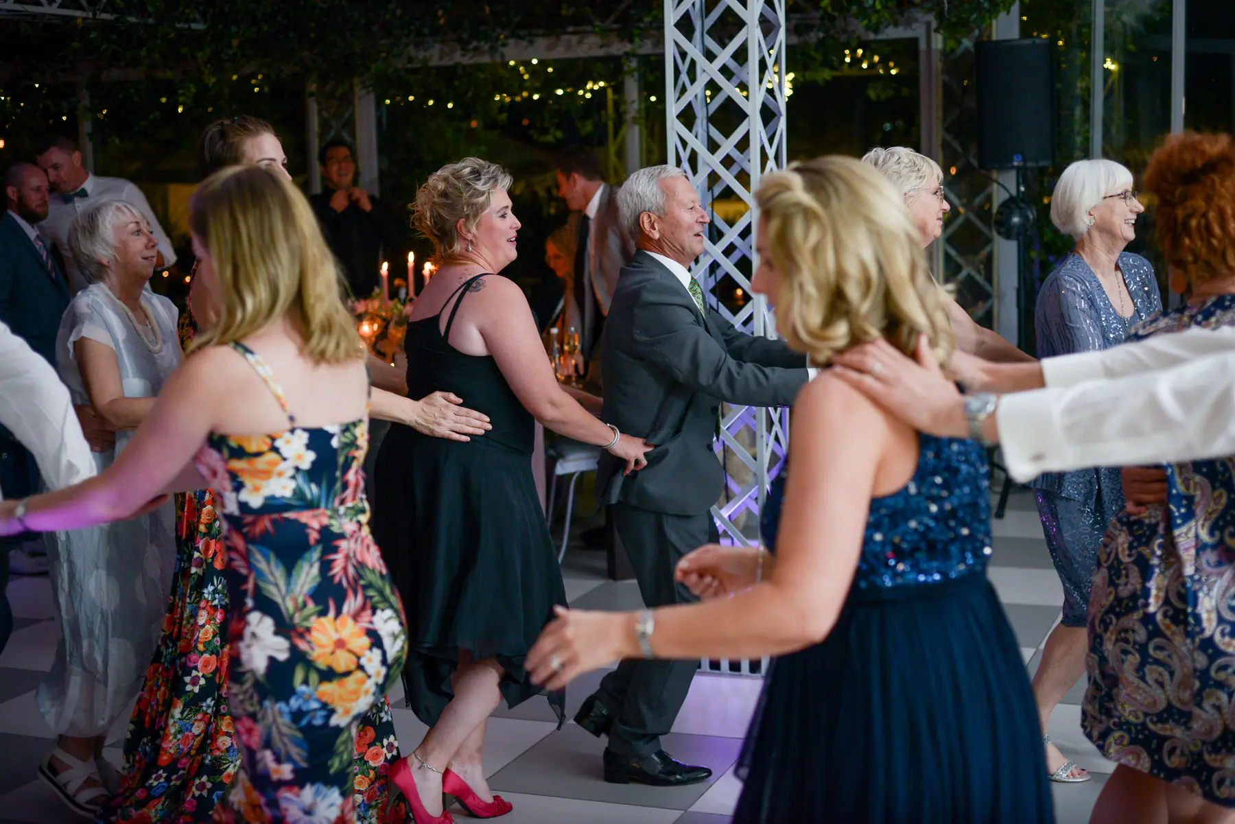 Wedding guests in a conga line with hands on waists, weaving past a purple-lit lattice pillar at a Paarl wedding