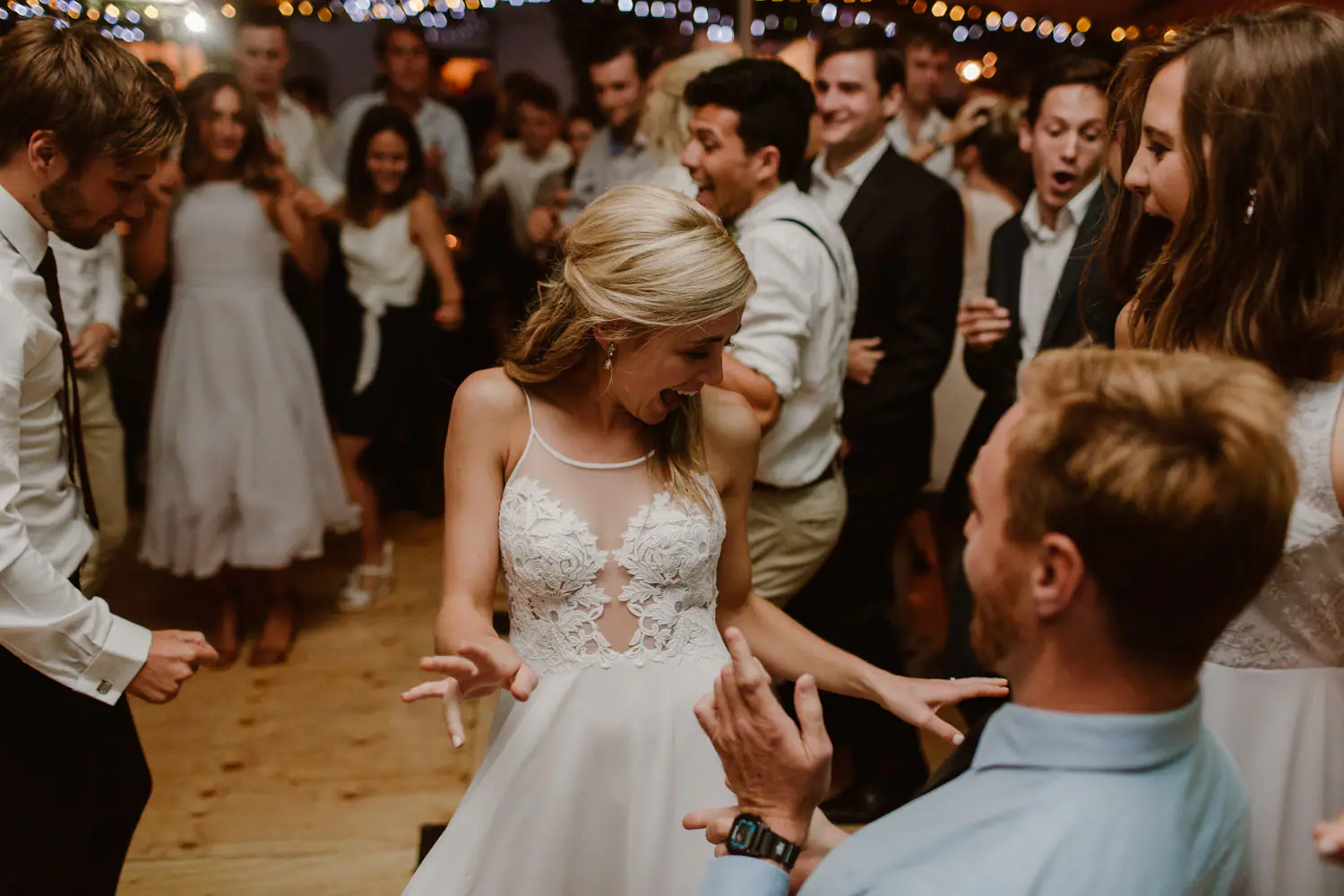 Sarah pulling a playful face as she dances inside a circle of clapping guests on a wooden dance floor
