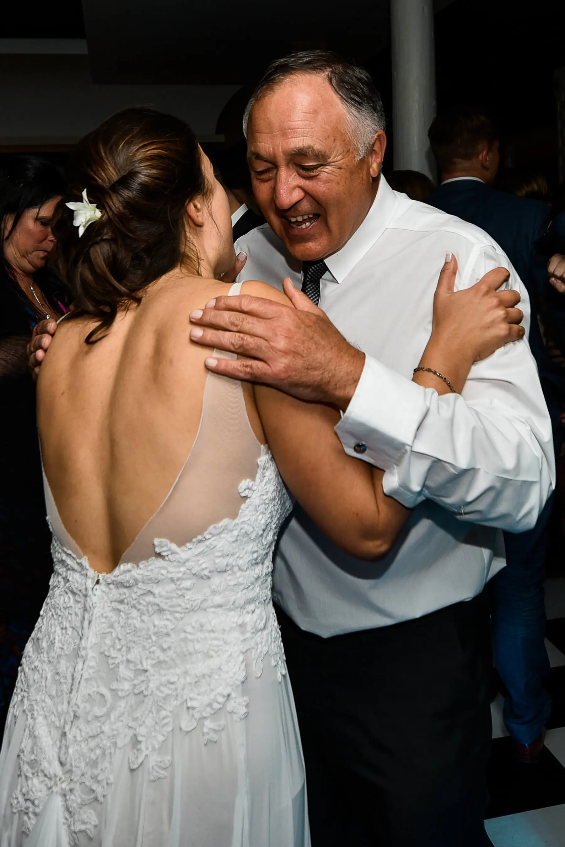 Karen in a backless lace gown embracing a laughing older man, his hand resting on her shoulder