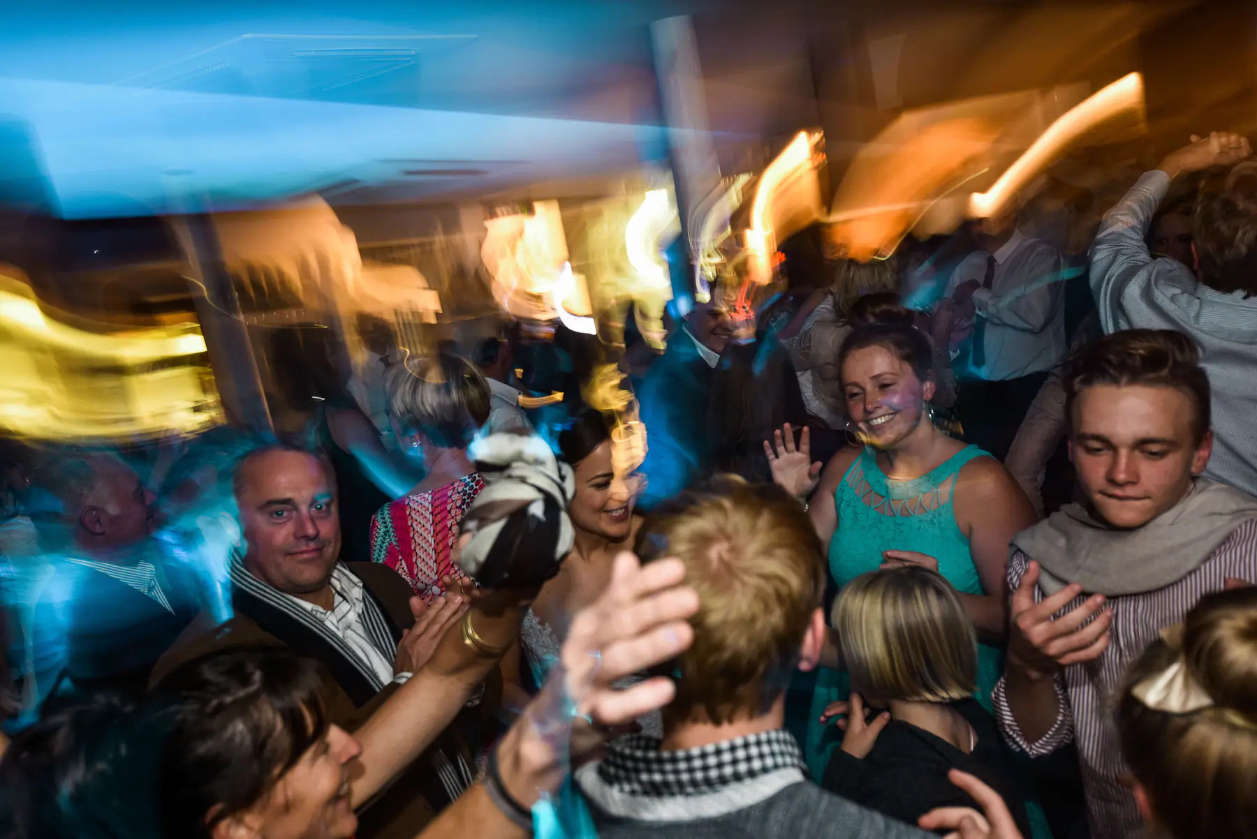 Karen smiling in a tight crowd of dancing guests as someone waves a striped scarf through orange and blue light trails