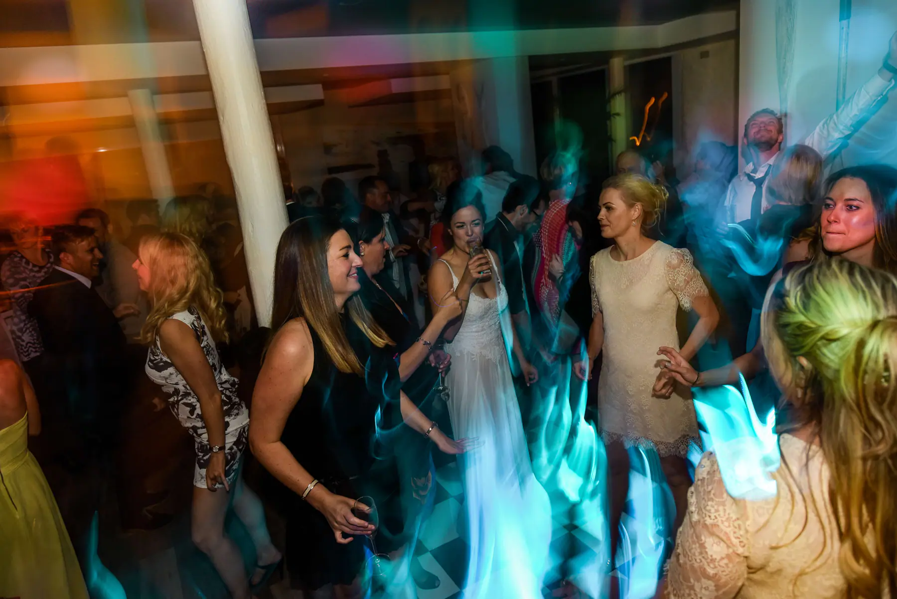 Karen sipping a drink as friends dance around her and a guest behind sings with one arm in the air