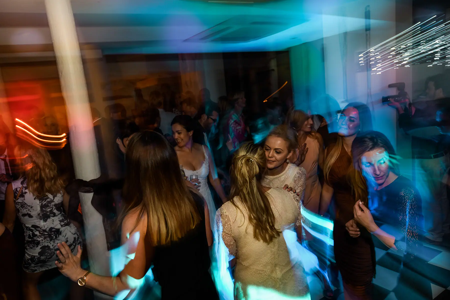 Guests dancing in a blur of teal, orange and white light trails as a videographer films at the edge of the floor