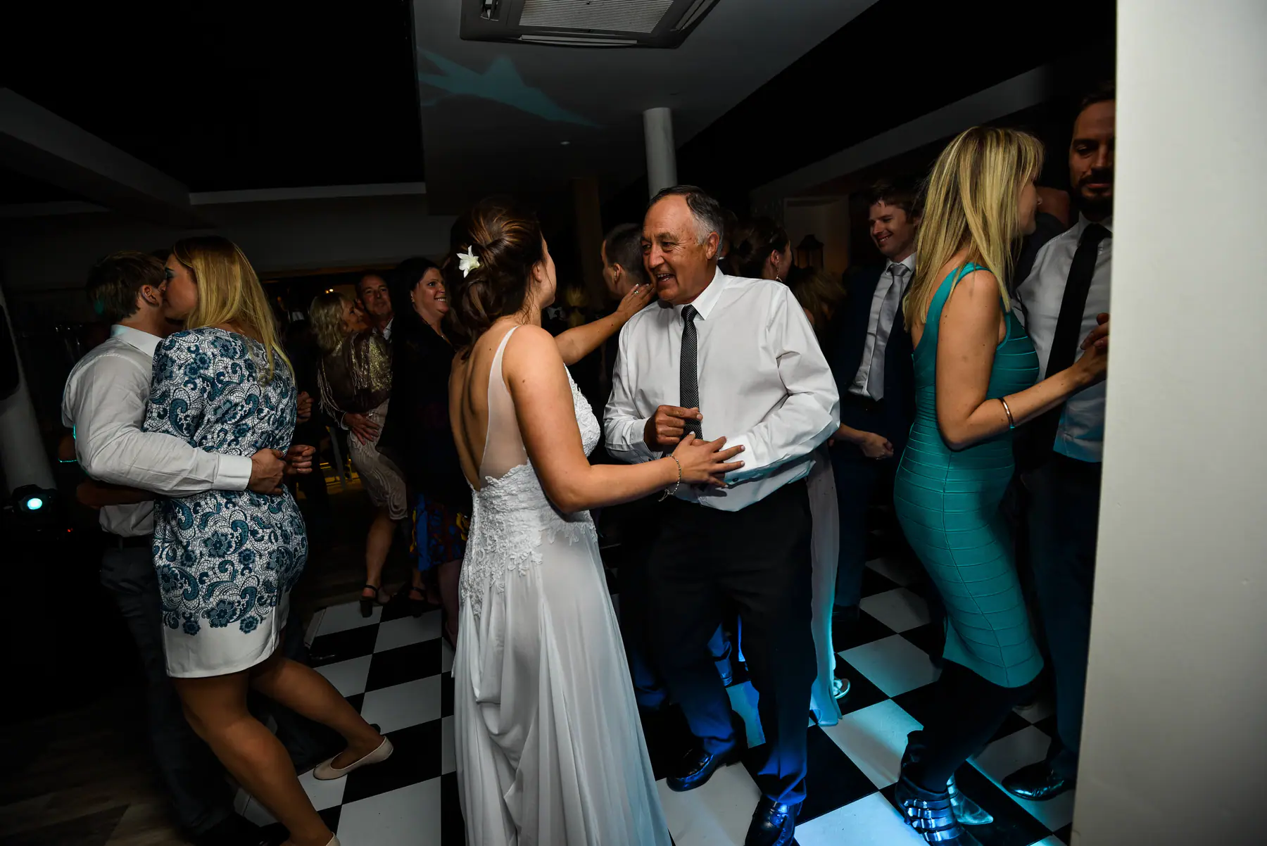 Karen dancing with a grey-haired man on the chequered floor as a couple embrace beside them