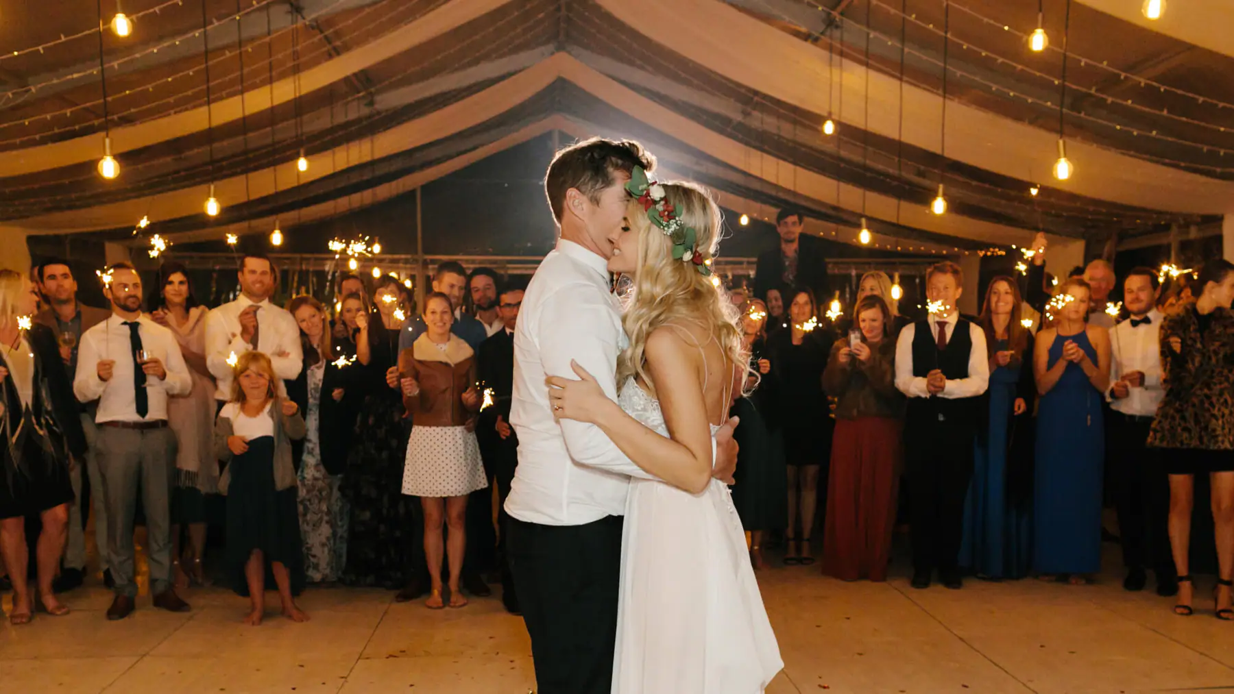 Mark and Louisa kiss during their first dance as guests hold sparklers in a marquee on a Stellenbosch olive farm