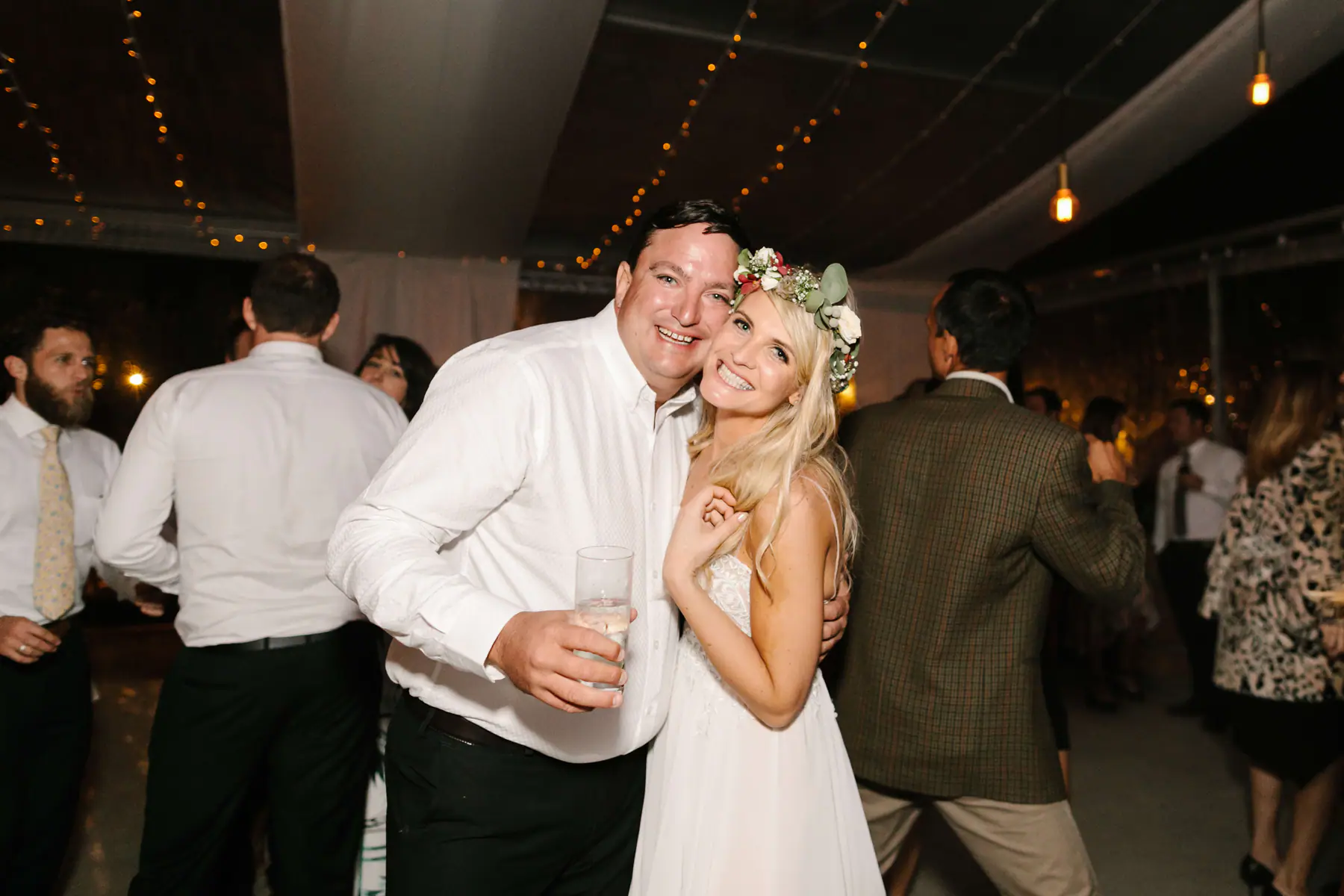 Louisa cheek to cheek with a smiling guest in a white shirt holding a drink on the dance floor