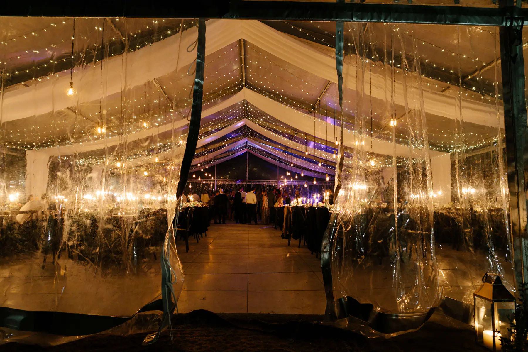 Marquee on the olive farm seen through its open doorway, fairy light canopies glowing over the tables and a lantern outside