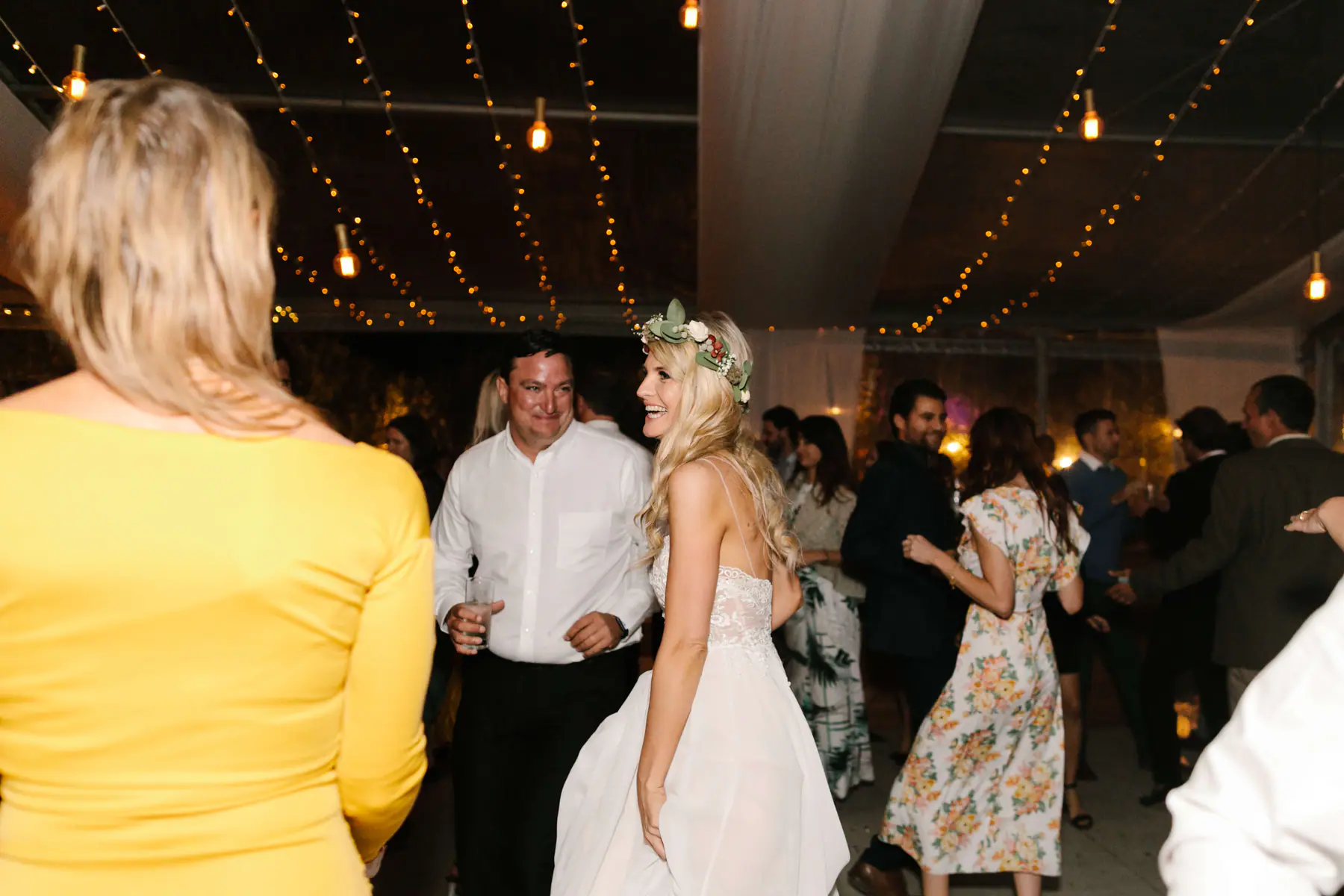 Louisa laughing over her shoulder on the dance floor as a guest in yellow and a man with a drink look on