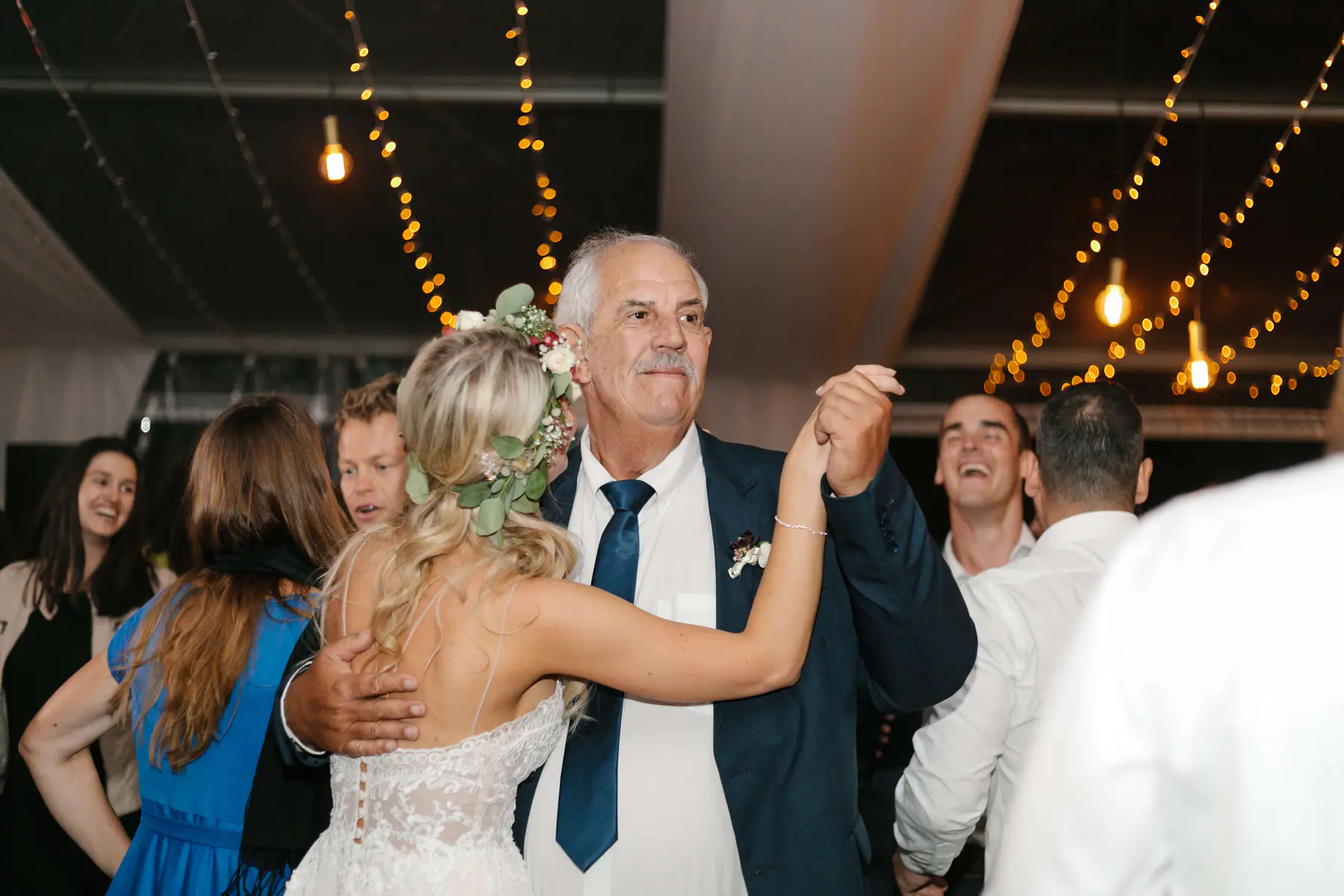 Louisa, seen from behind in her flower crown, dancing hand in hand with an older man wearing a buttonhole