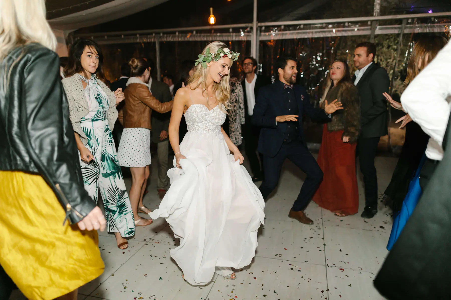 Louisa in a flower crown dancing on confetti as a bearded guest in a bow tie dances opposite her