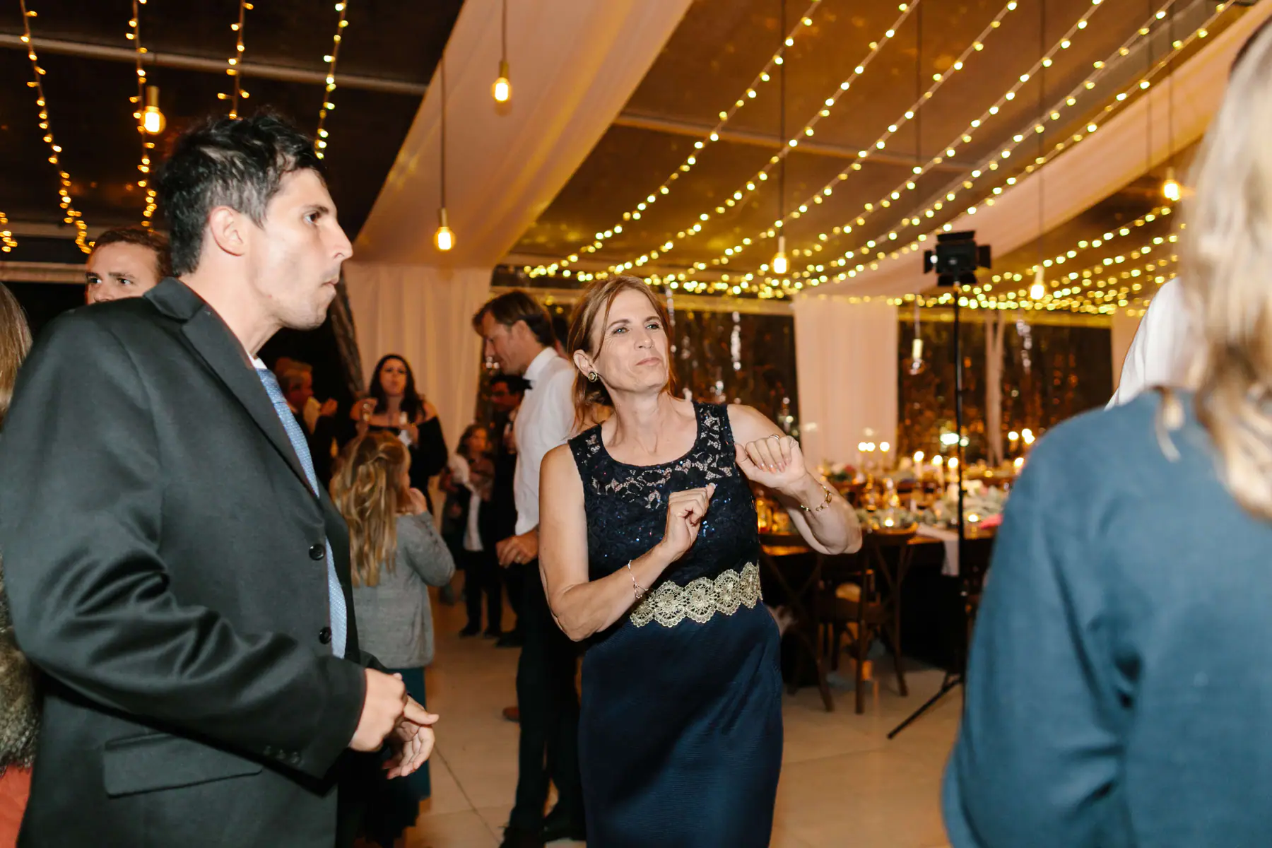 Woman in navy lace with a gold beaded waist dancing with her fists up beside a man in a dark suit