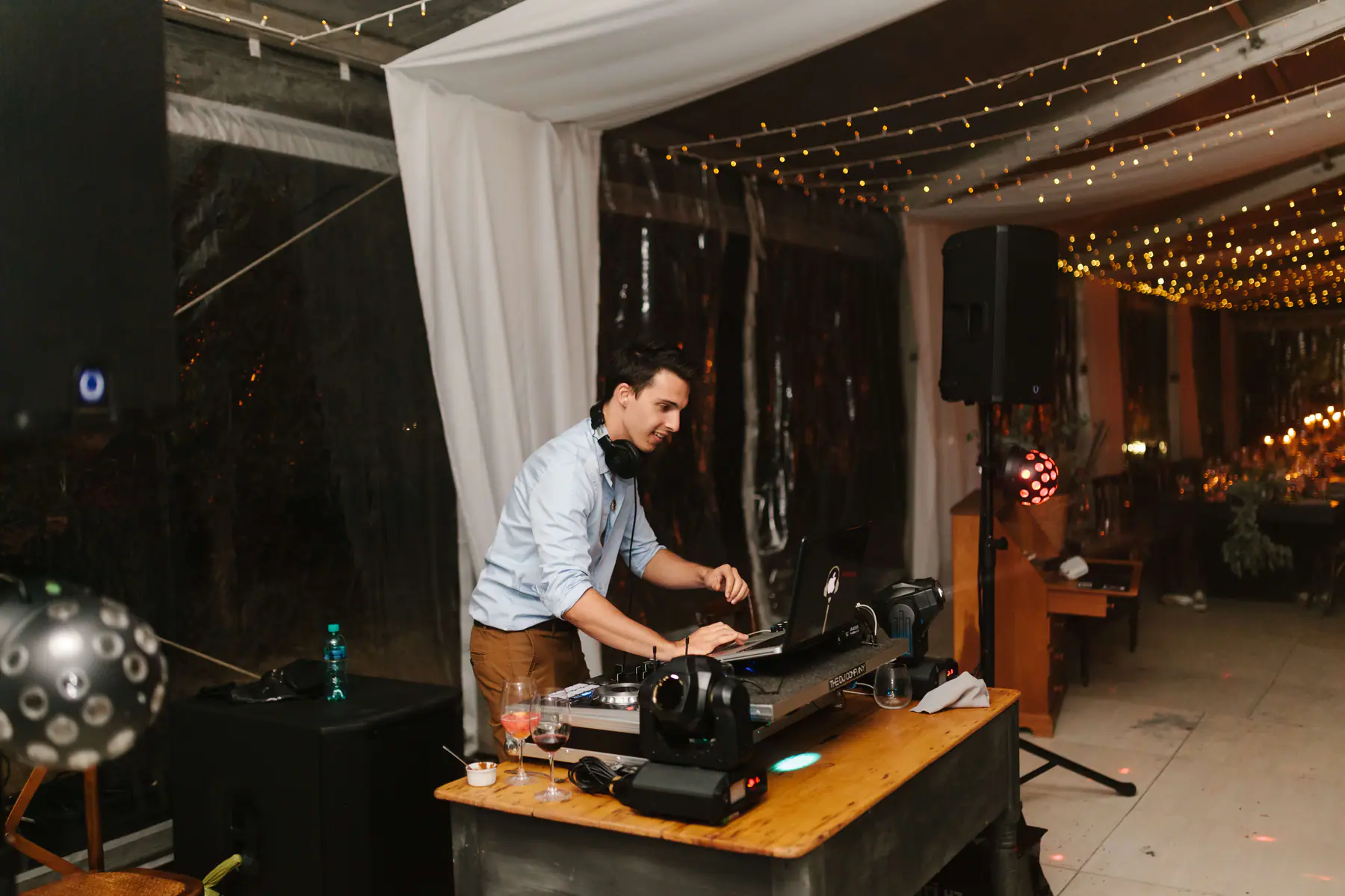 Stellenbosch wedding DJ mixing at a wooden booth with moving head lights, a speaker on a stand and LED effect lights
