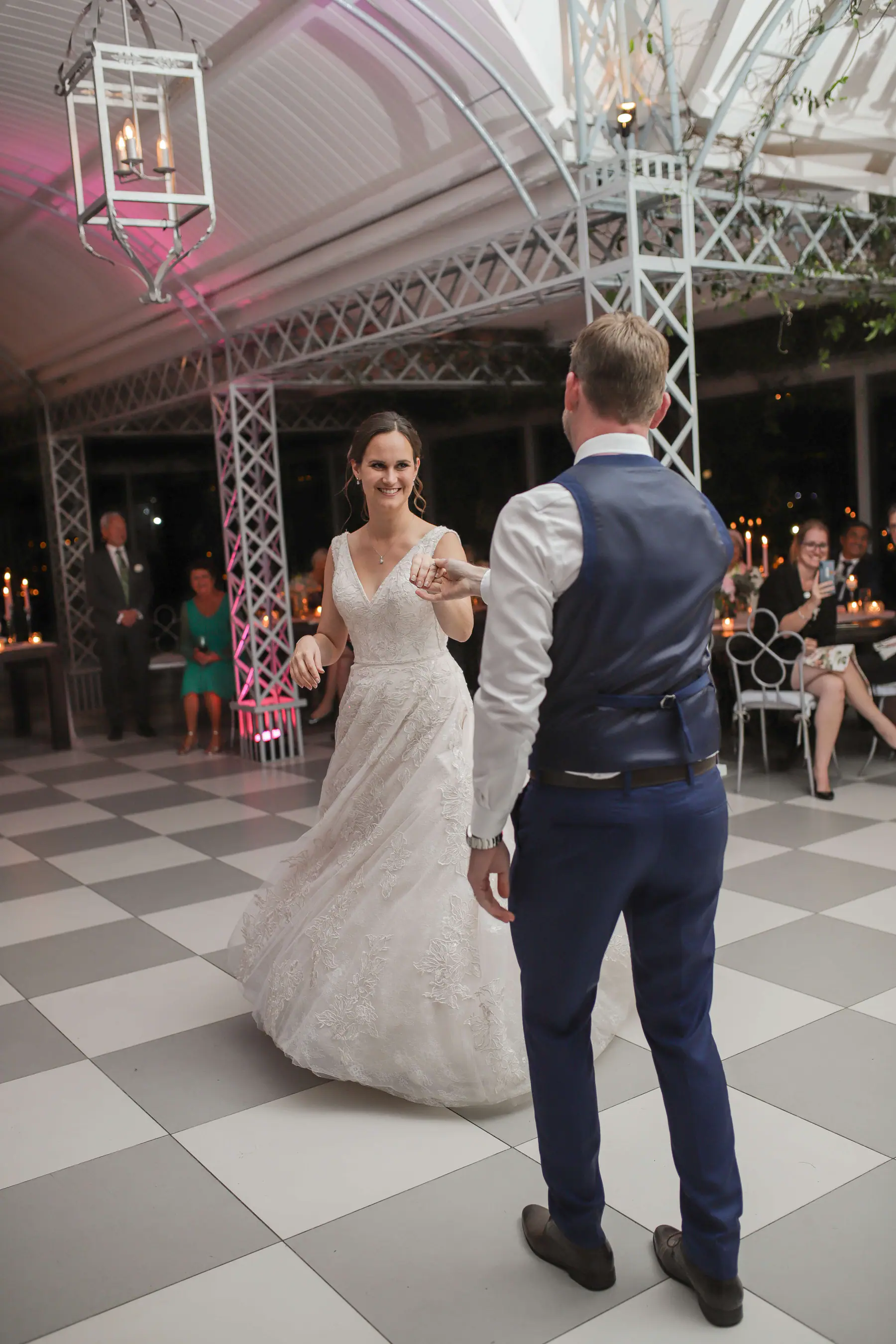Scott leading Dora into a twirl during their first dance, a pink uplighter glowing at the foot of a lattice pillar