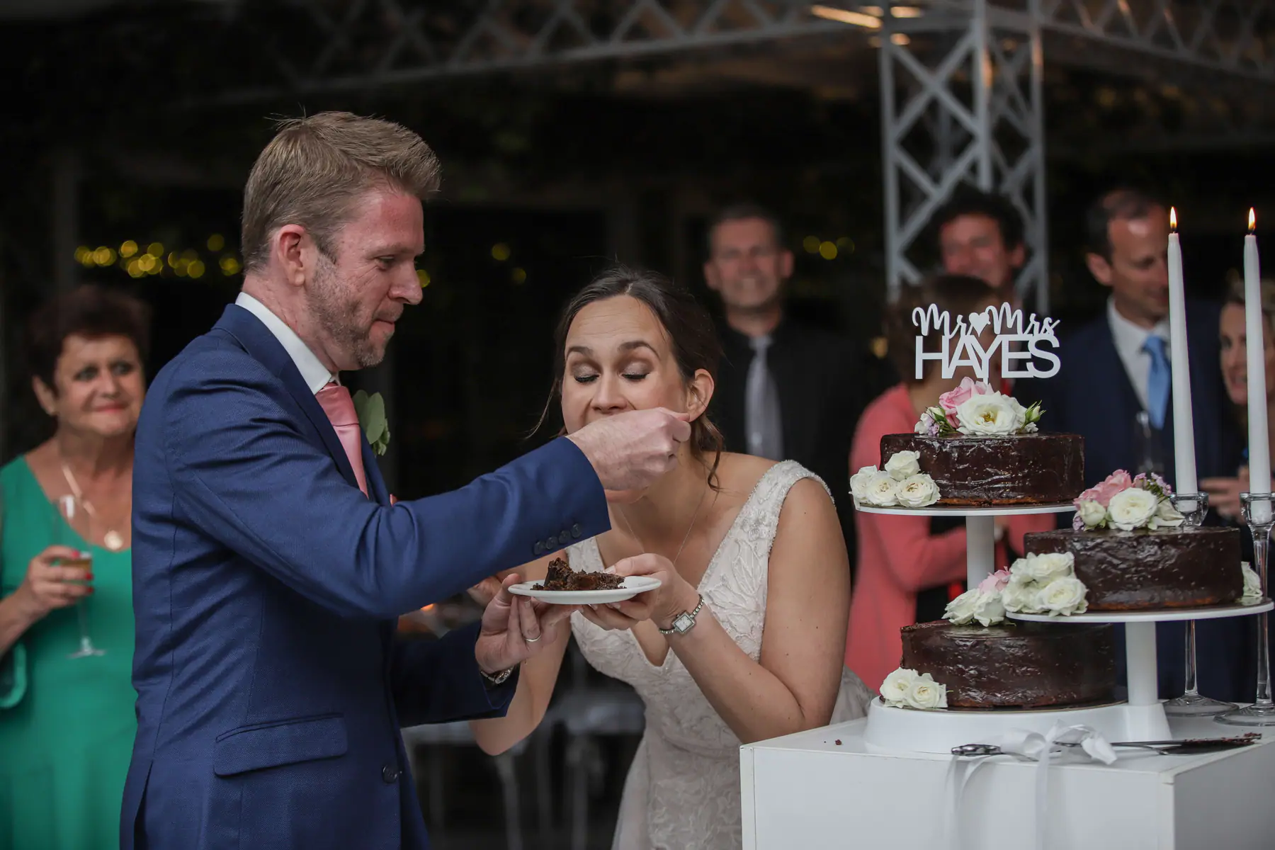 Scott feeding Dora a bite of their chocolate wedding cake, its tiers topped with white roses and a Mr and Mrs sign
