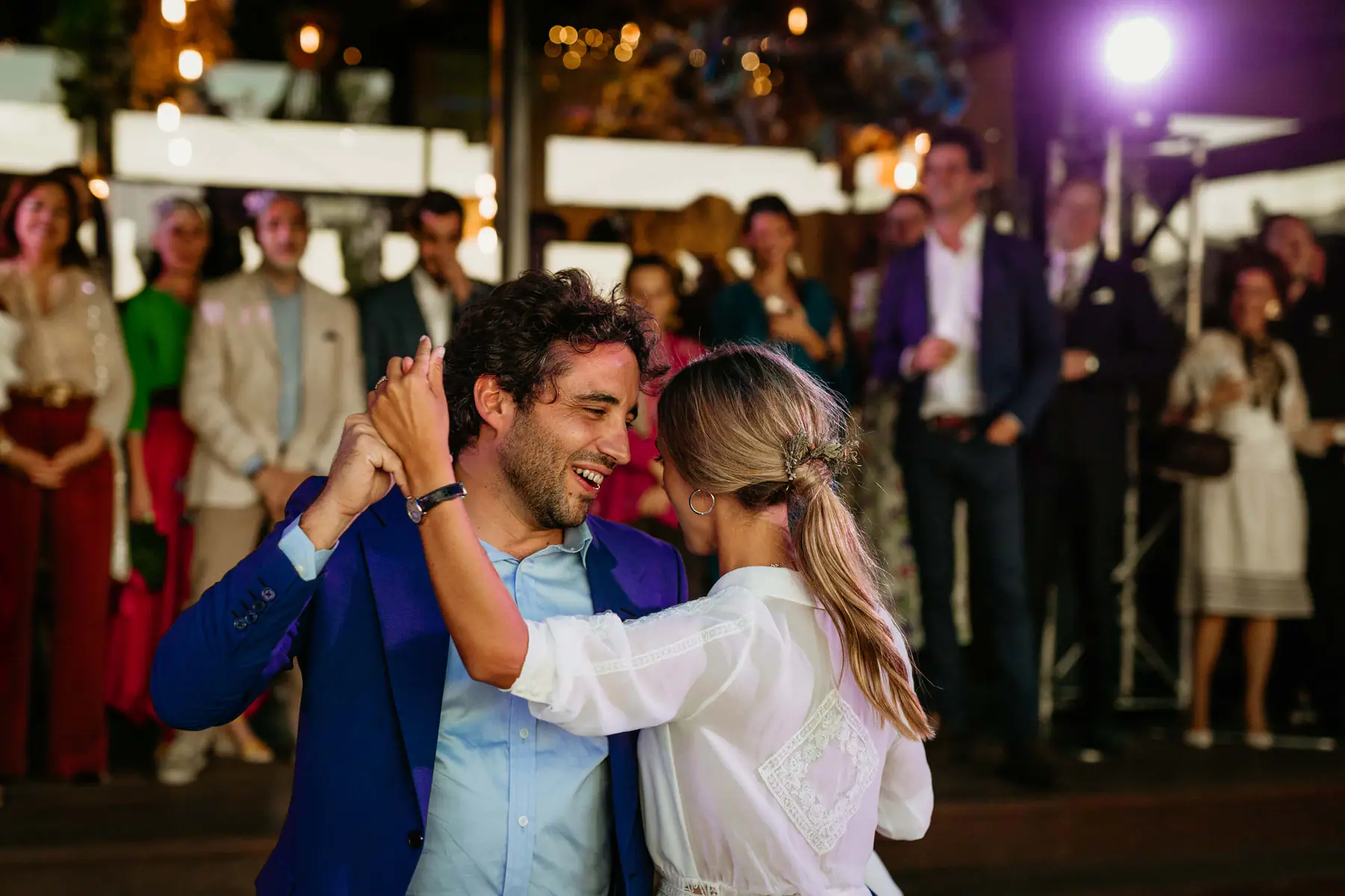 Mario spins Barbara on the dance floor under a purple spotlight on a lighting truss as guests look on