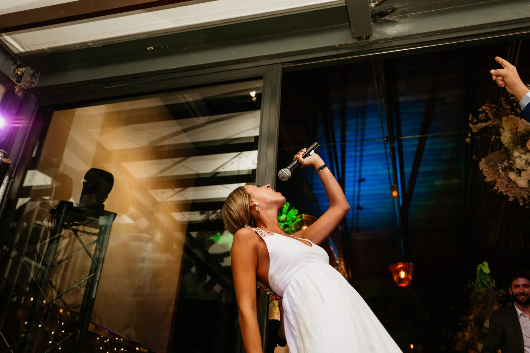 Barbara leans back to sing into a microphone beside a moving head light on a truss, purple light flaring at the left