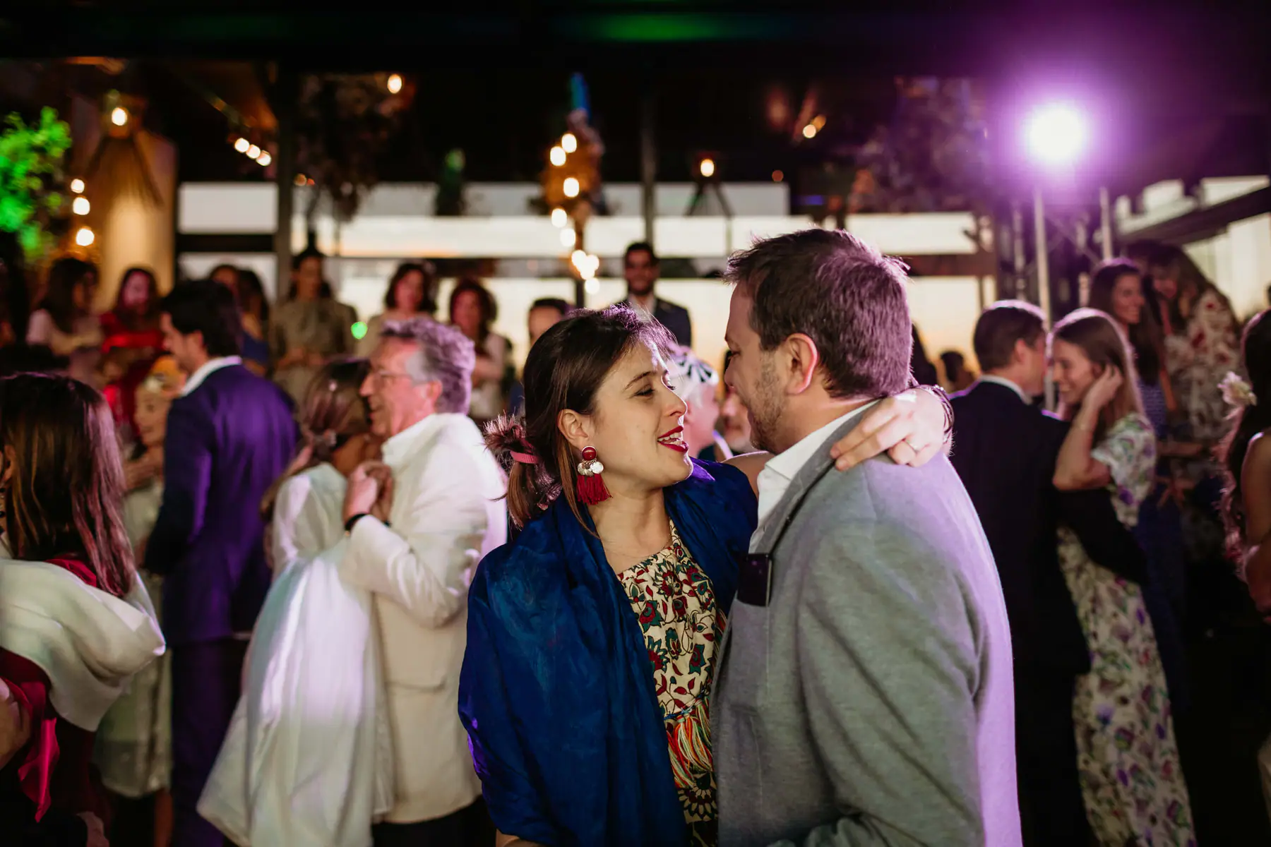 Guests in a blue shawl and a grey blazer dance close under a purple spotlight at Tokara in Stellenbosch