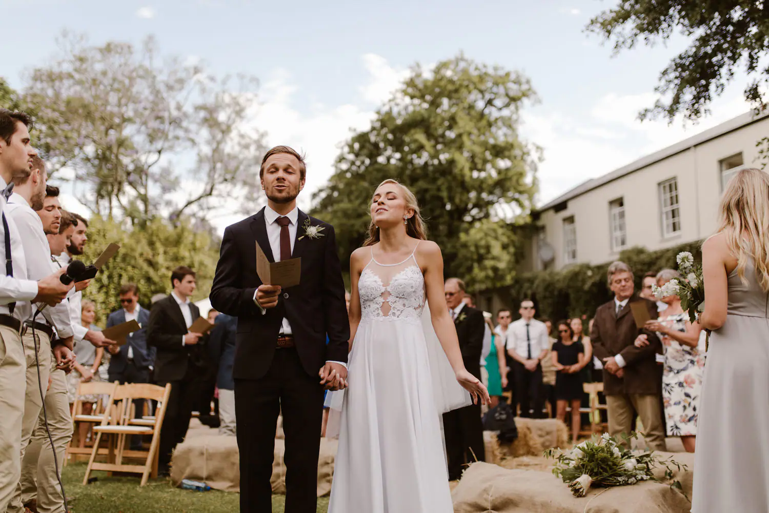 Ramsay and Sarah singing hand in hand from song sheets at their garden ceremony at Pam Golding's estate
