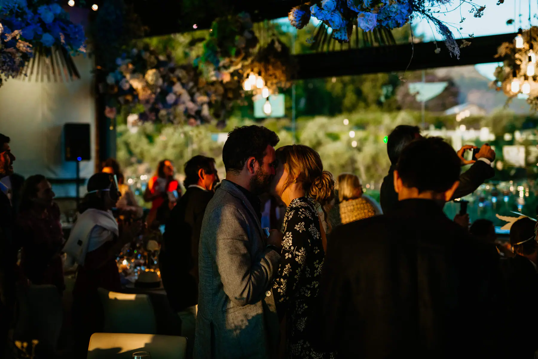 Two guests kiss under hanging blue hydrangeas as evening sun lights the hillside view through Tokara's glass walls