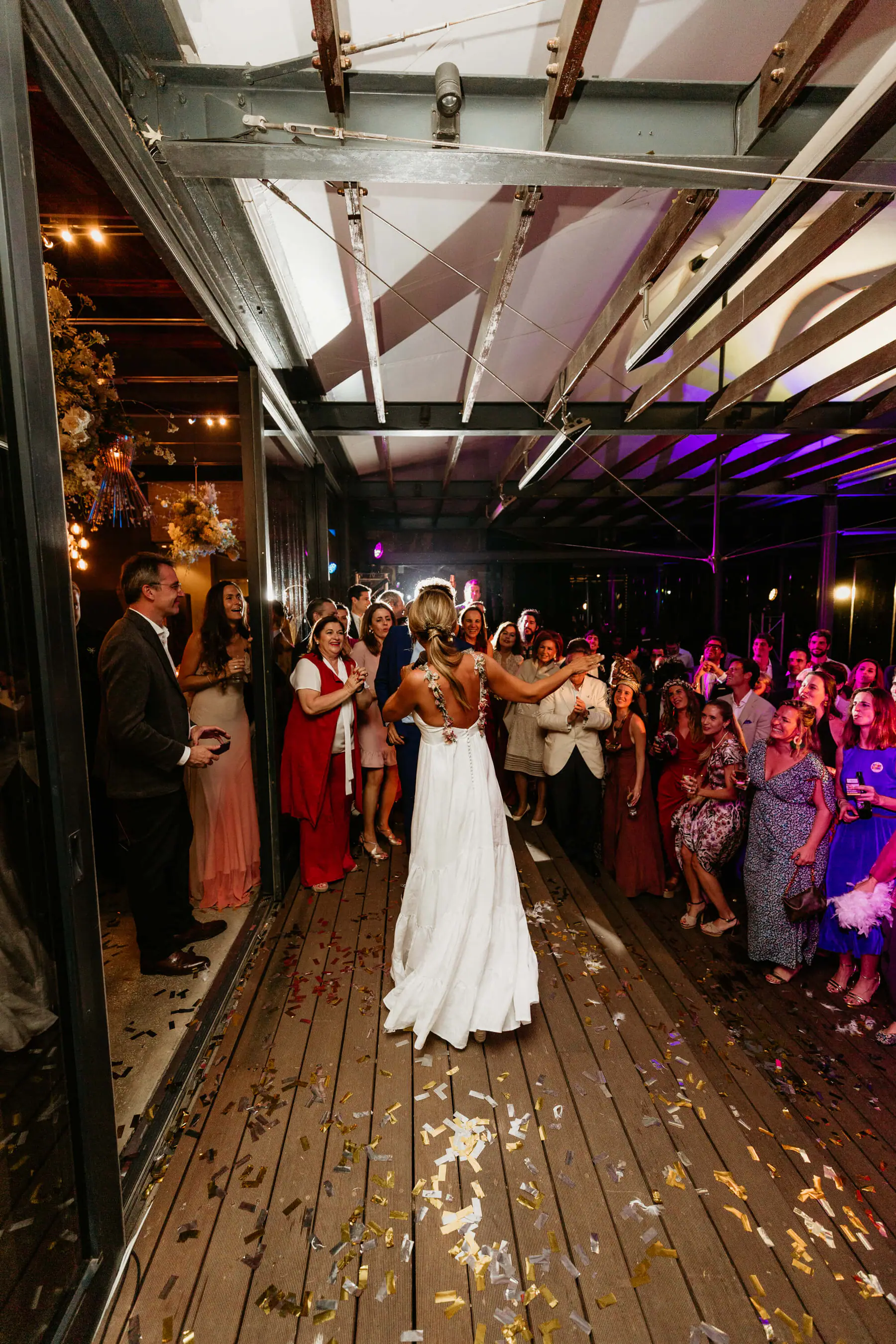 Barbara, seen from behind in a long white gown, opens her arms to cheering guests on a confetti-strewn deck at Tokara