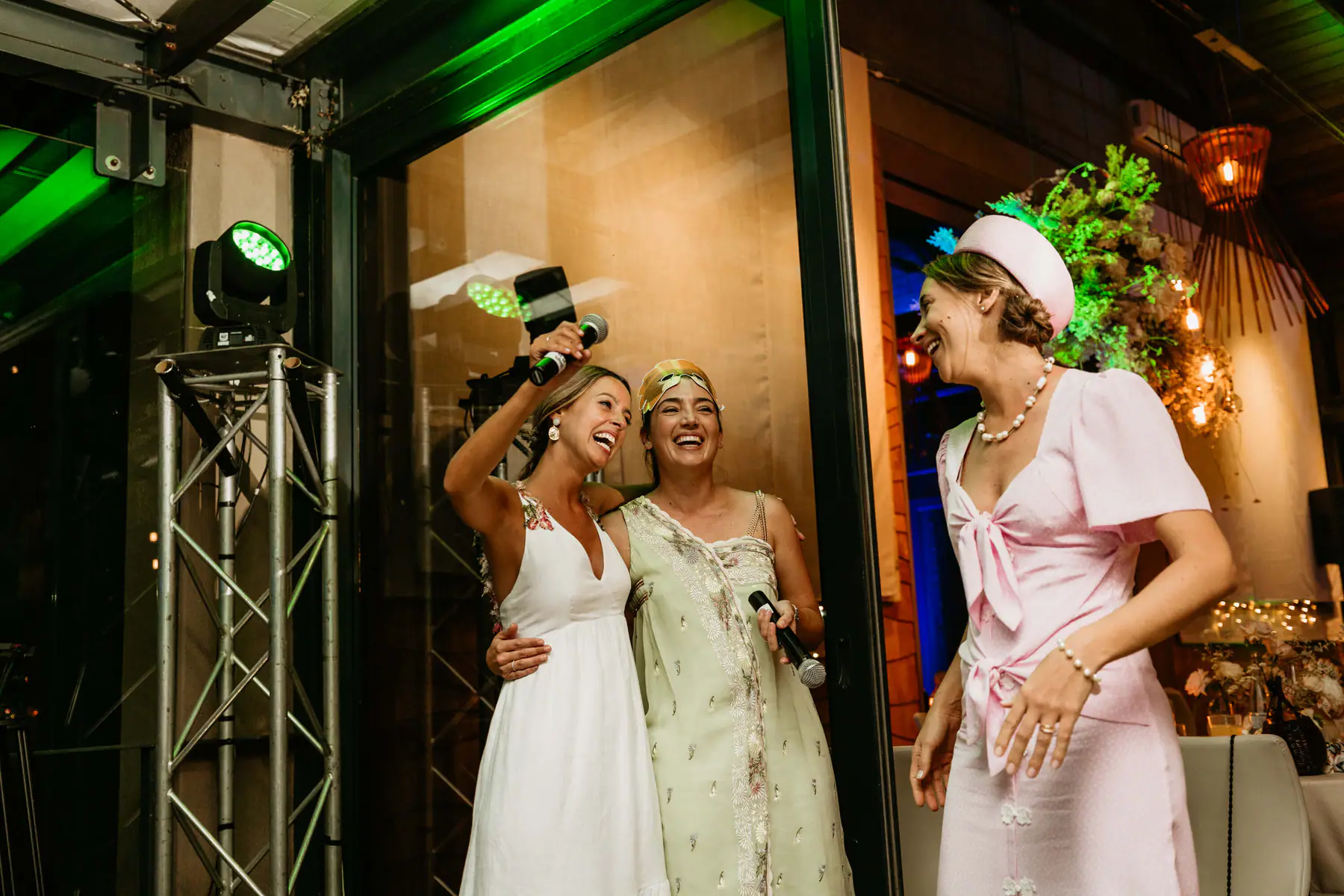Barbara and a friend in a gold headband laugh with microphones beside The DJ Company's green moving head on a truss