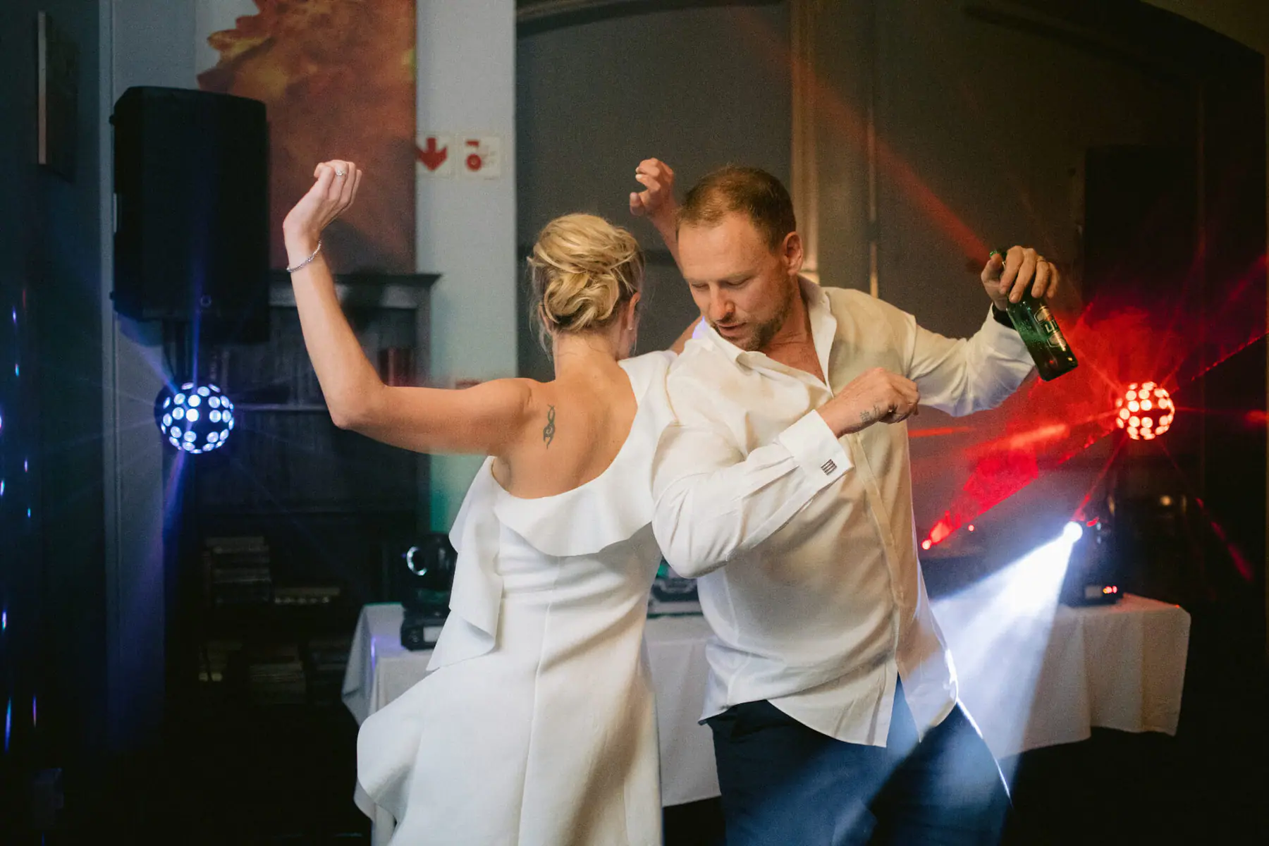 Kirsten and Greg dance with arms raised under The DJ Company's red and blue party lights at Simon's, Groot Constantia