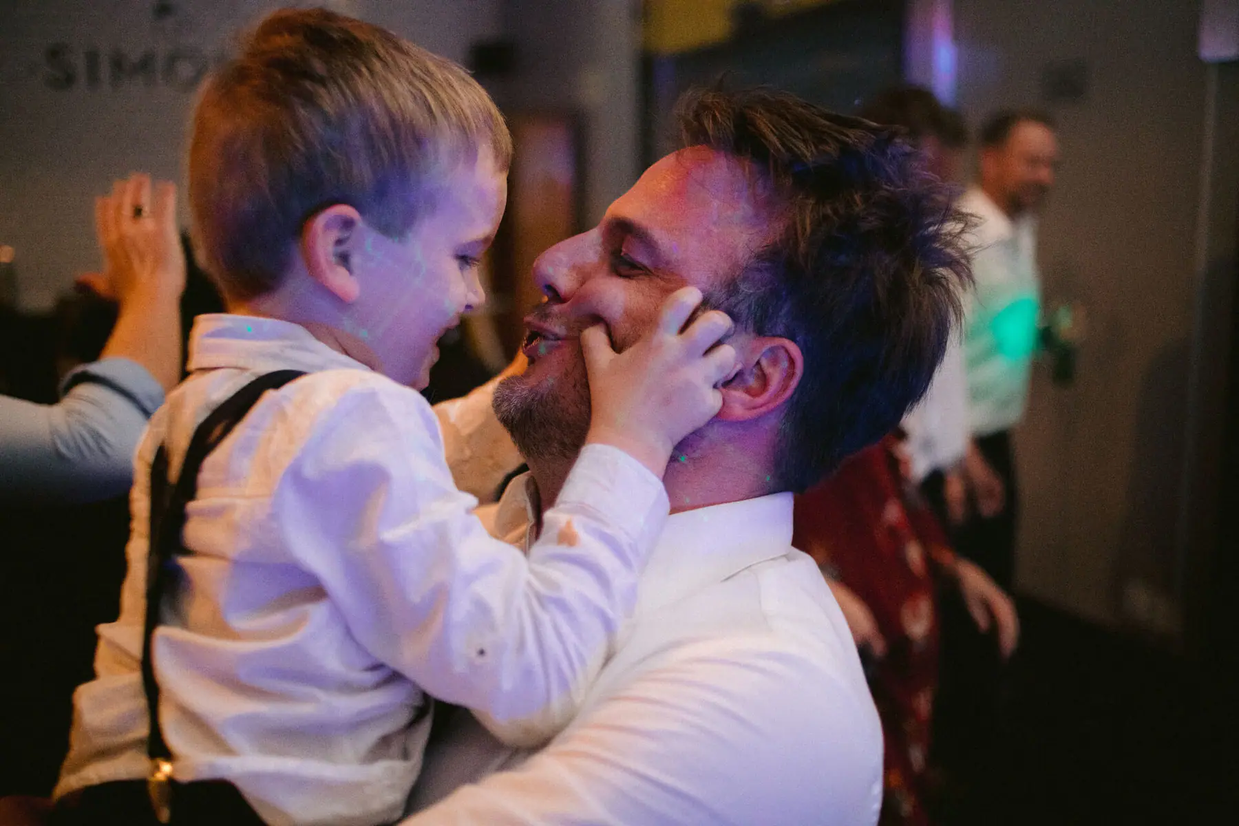 A young guest in a white shirt and braces squeezes a smiling man's cheeks at Simon's Restaurant