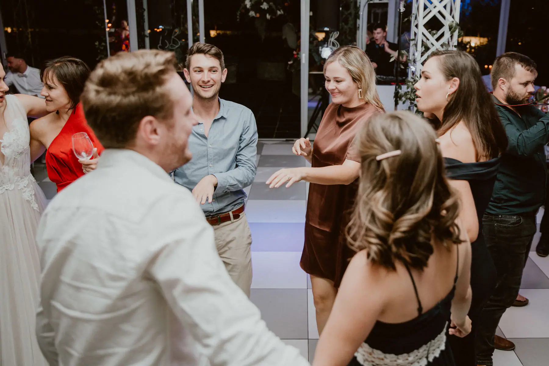 Guests dancing on the chequered floor, a man in a blue shirt and a woman in brown satin, as the DJ sings along at his booth