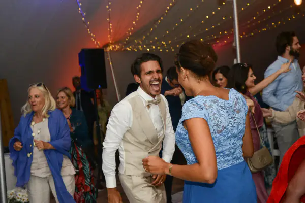 Laughing groom dancing with his guests at a marquee wedding reception