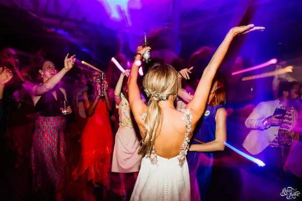 Bride with her arms in the air dancing under purple and red party lights