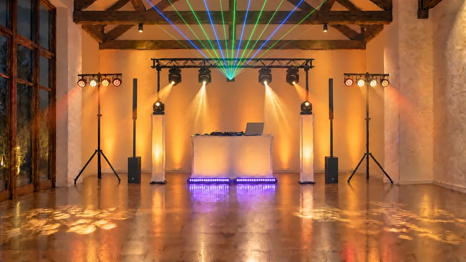 Dance floor in warm light: a lighting bridge with moving heads and a laser, PAR lights, column speakers and a white booth