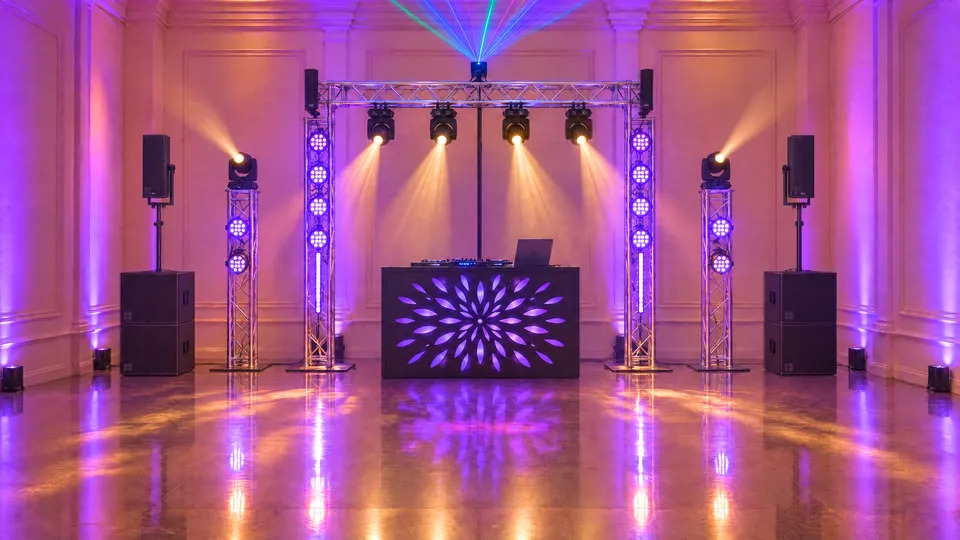 Dance floor in purple: a truss goalpost with moving heads and a laser, d&b speakers on subwoofers and a black DJ booth