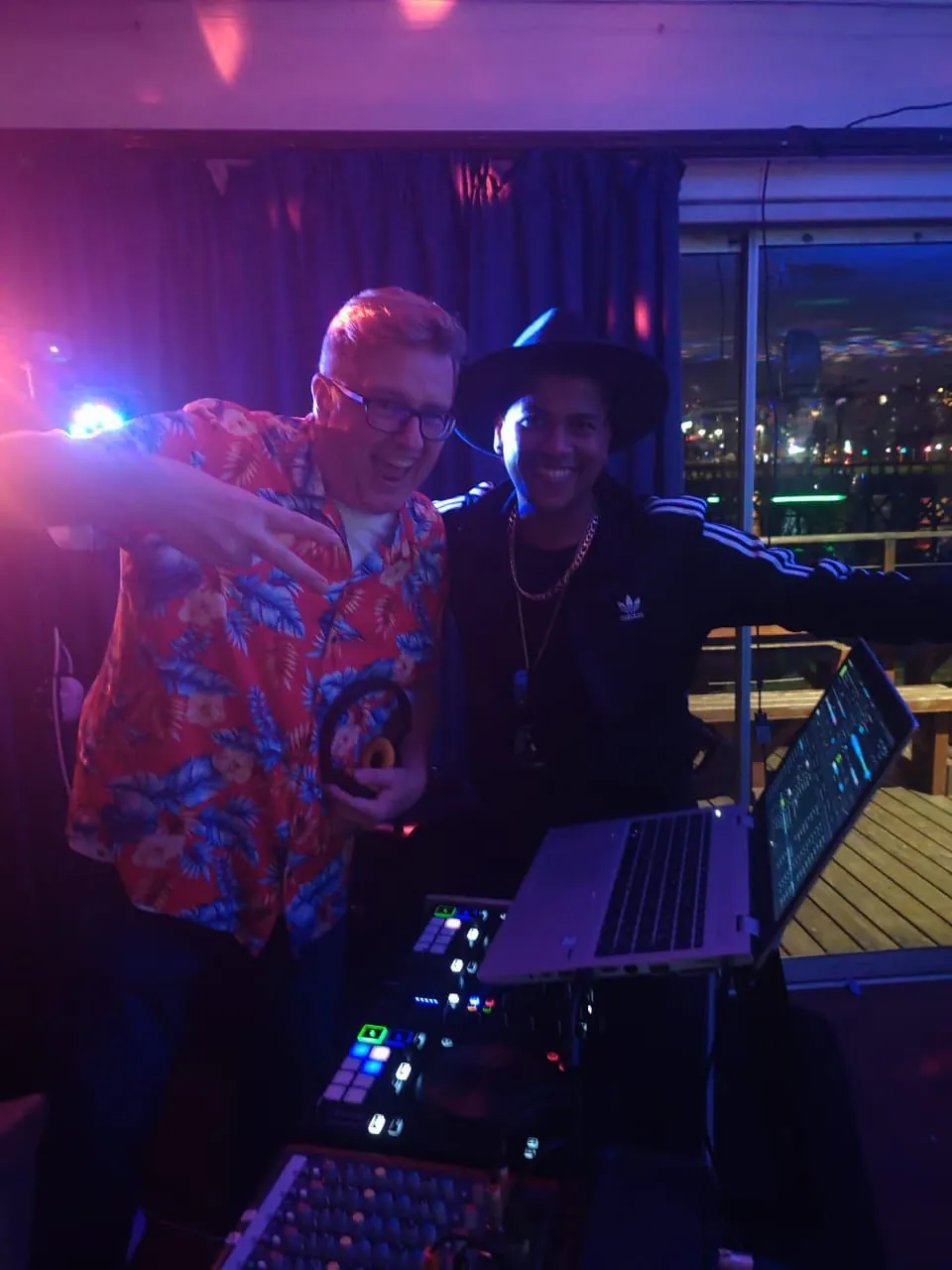 Greig and the host at the DJ booth under purple party lights