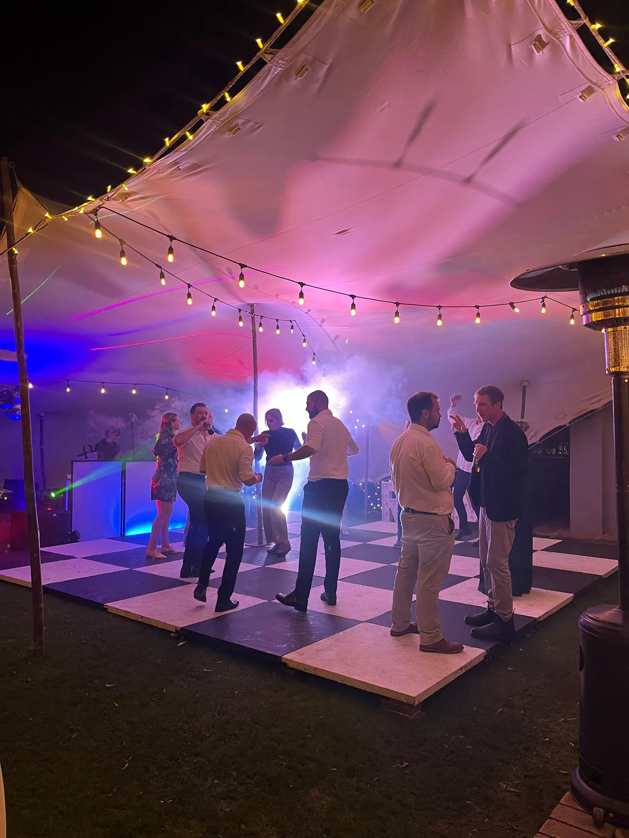 Guests dancing on a black and white floor under a stretch tent with string lights