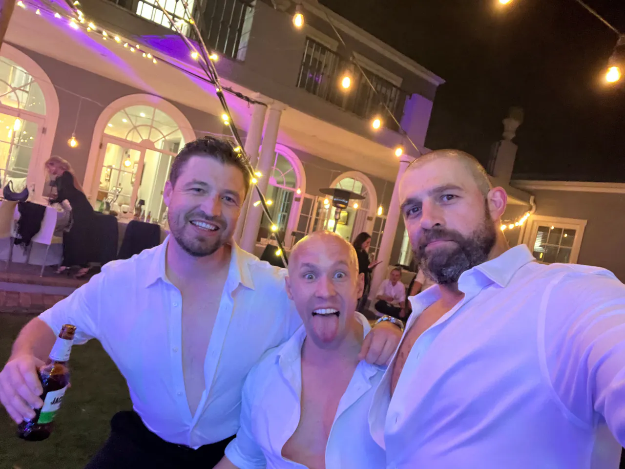 Three guests in white shirts smiling for a selfie on the lawn at the wedding