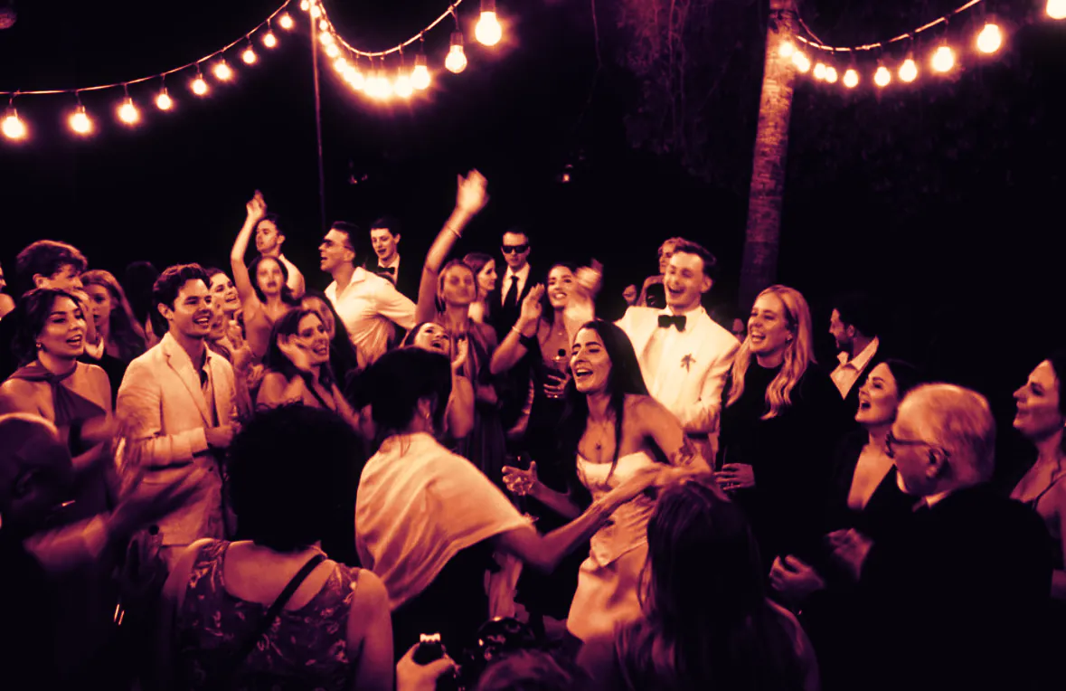The bride, the groom and their guests singing and dancing under string lights at night